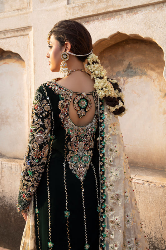 Woman in traditional embroidered outfit with floral hair accessories, standing against a stone wall.