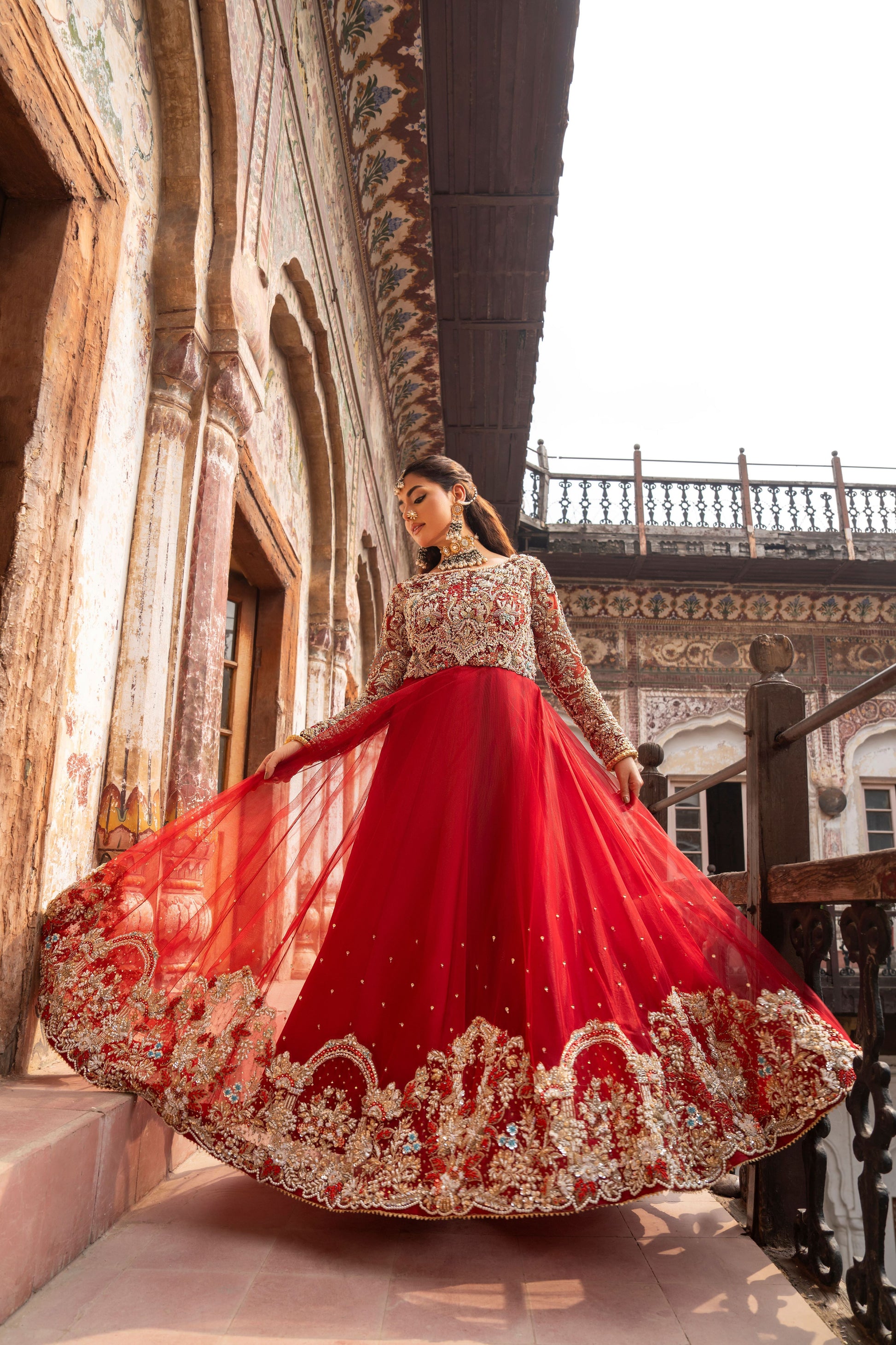 Woman in a red and gold traditional outfit standing in front of an ornate architectural background.