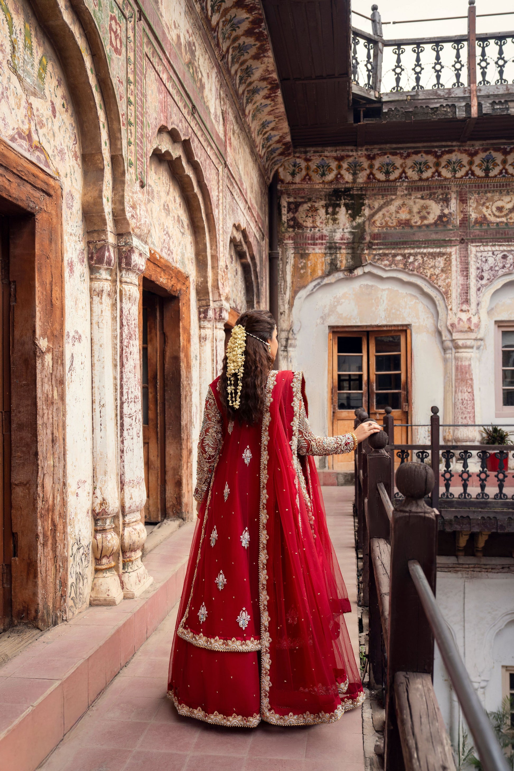 Woman in a red traditional outfit standing in an ornate courtyard.
