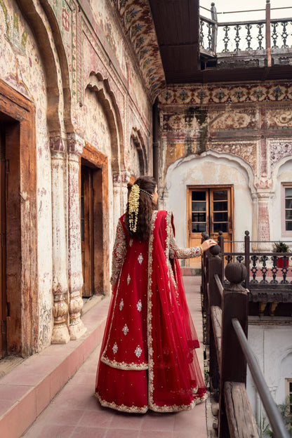 Woman in a red traditional outfit standing in an ornate courtyard.