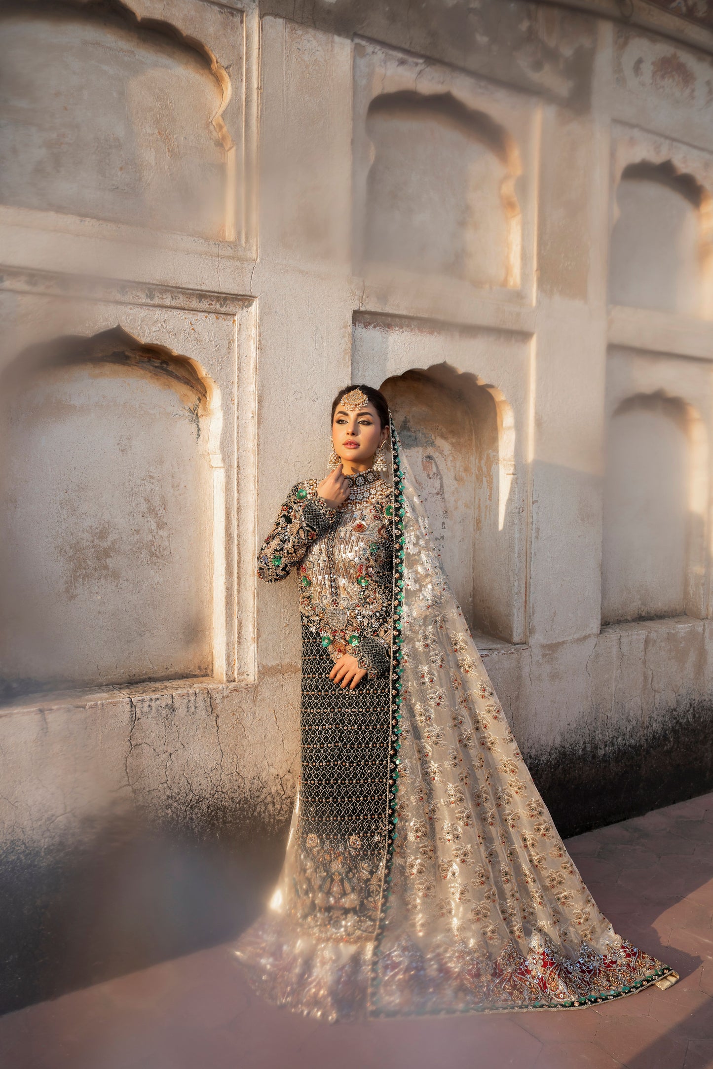 Woman in traditional attire standing in front of a stone wall with arched niches.