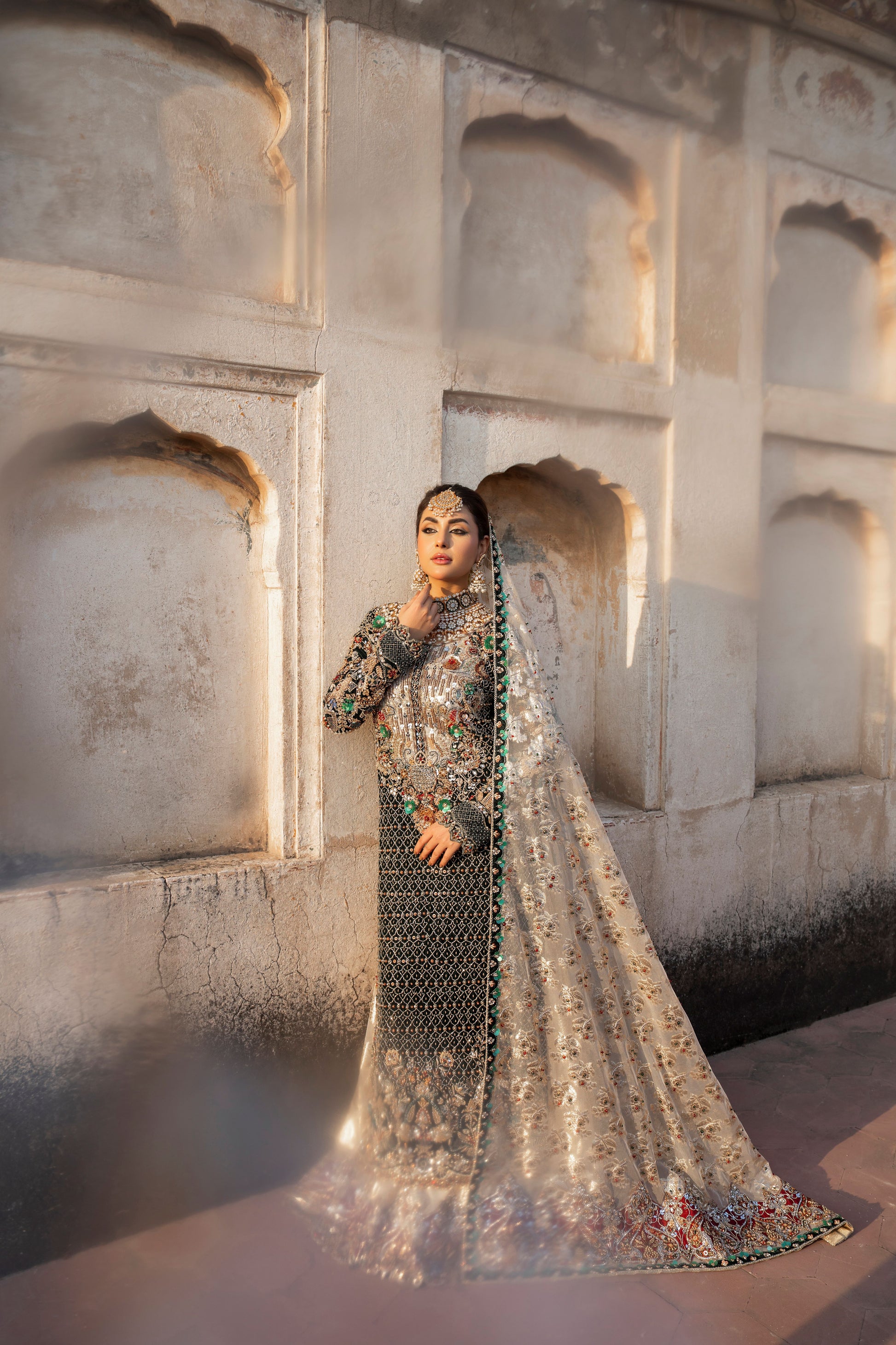 Woman in traditional attire standing in front of a stone wall with arched niches.