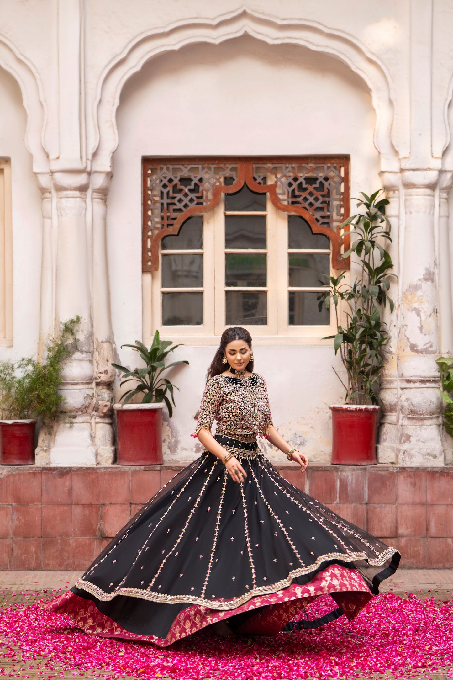 Woman in traditional black and gold outfit standing in front of an architectural building with plants.