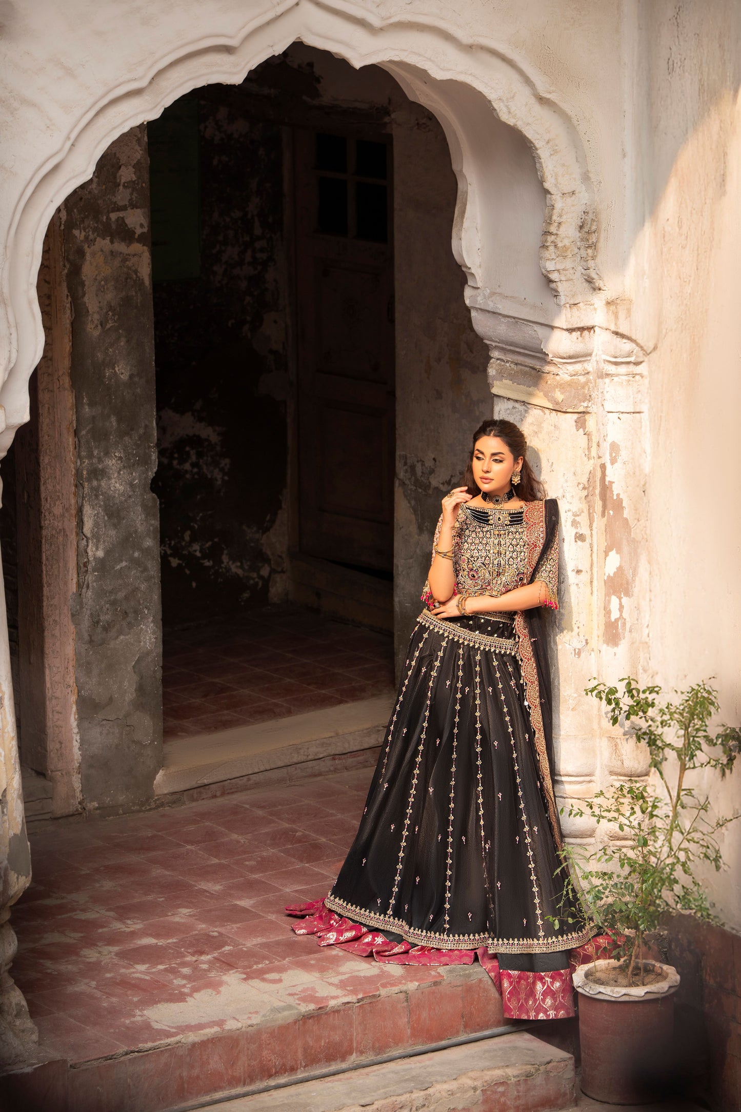 Woman in traditional black and red outfit standing in an archway with decorative elements.