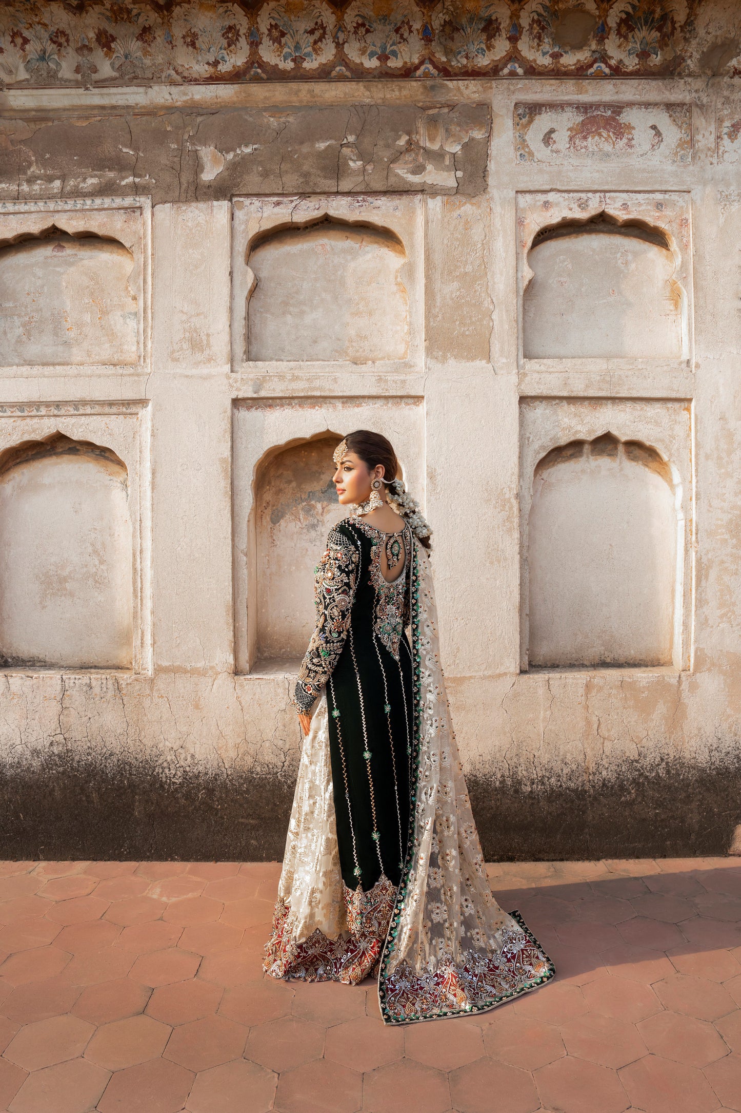 Woman in traditional attire standing in front of an architectural wall with arched windows.