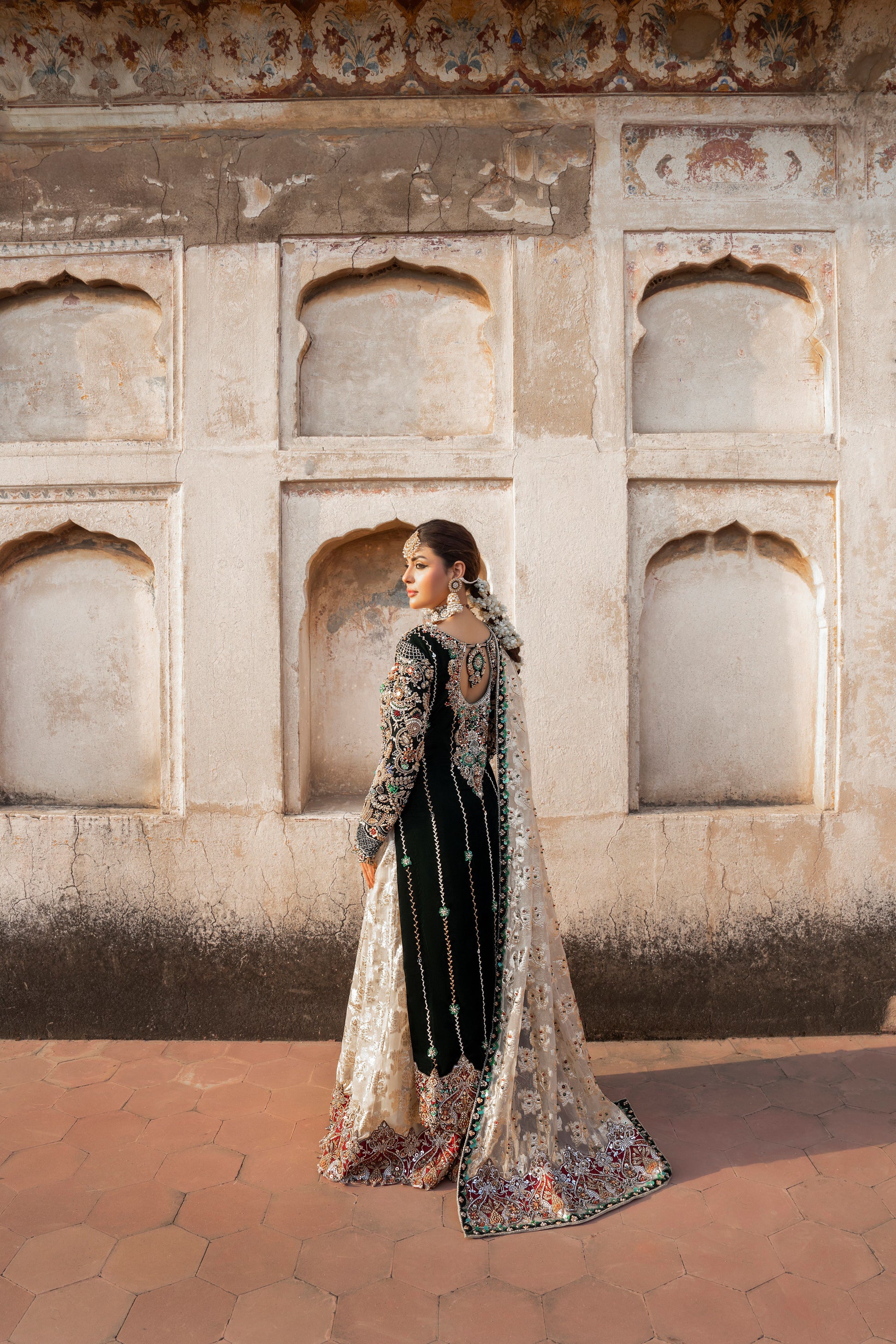 Woman in traditional attire standing in front of an architectural wall with arched windows.