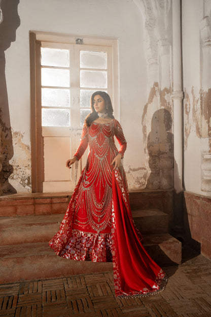 Woman in a red and gold traditional outfit standing in a room with decorative walls.