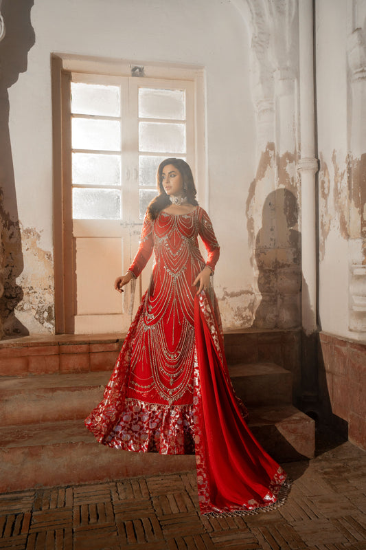 Woman in a red and gold traditional outfit standing in a room with decorative walls.