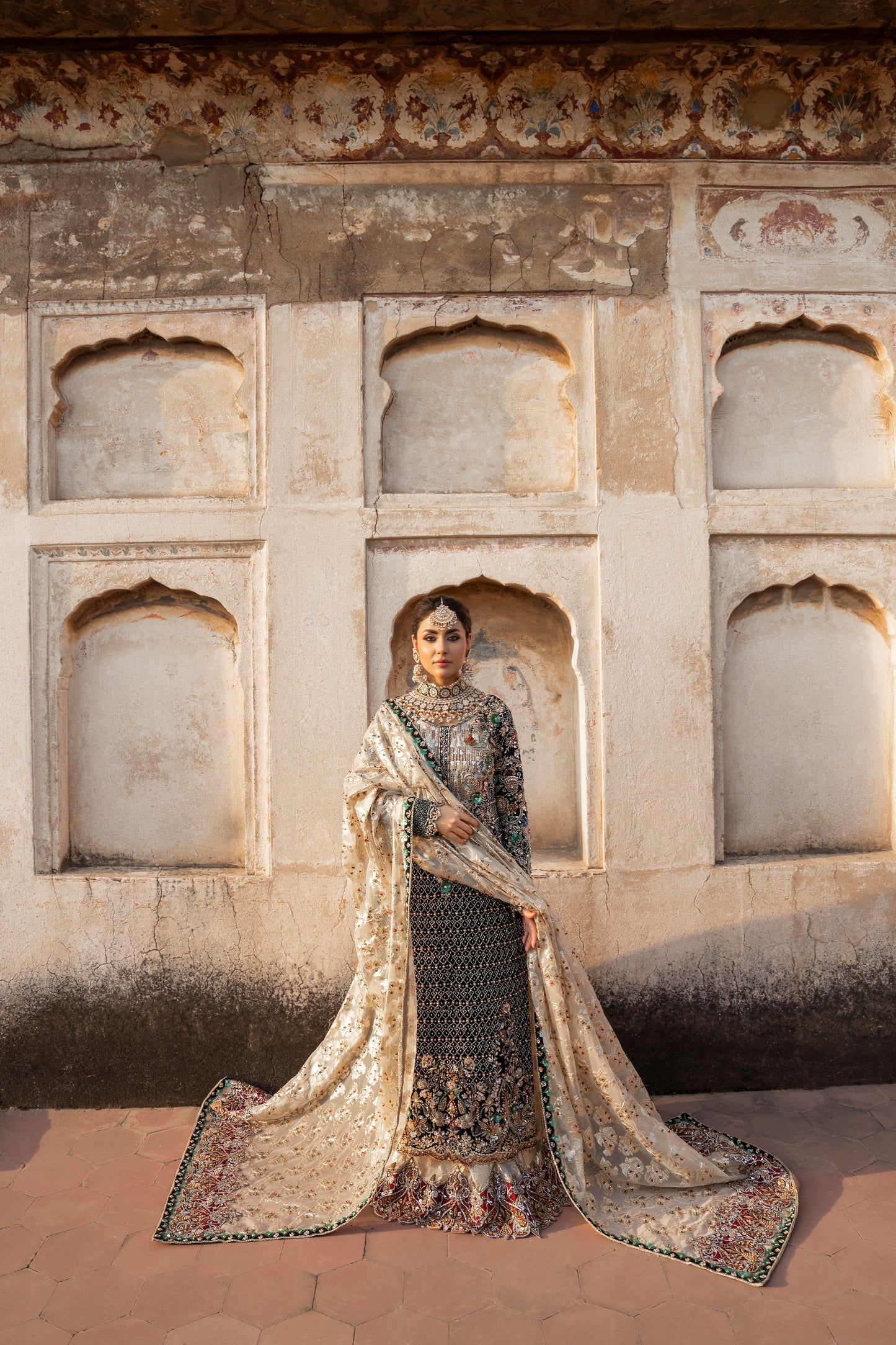 Woman in traditional attire standing in front of an architectural wall with arched niches.