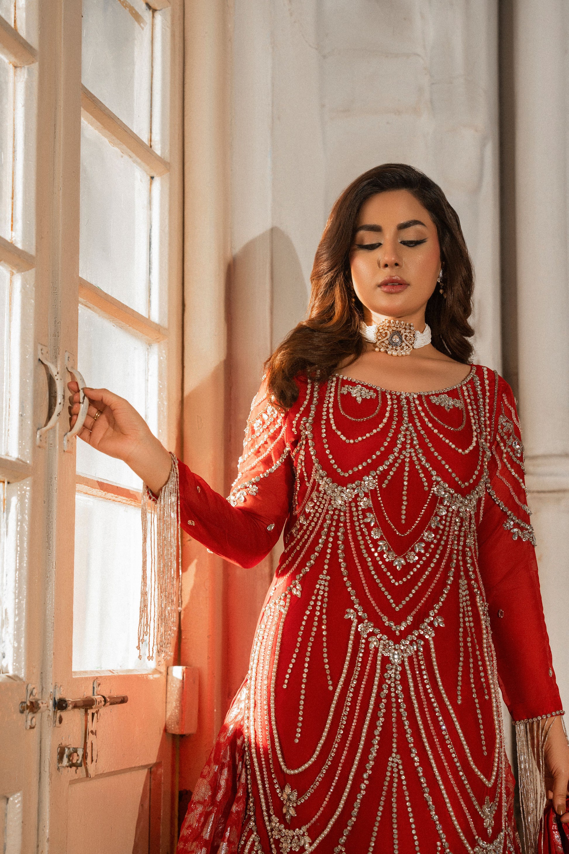 Woman in a red and silver traditional outfit standing in a sunlit room.