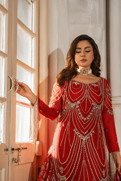 Woman in a red and silver traditional outfit standing in a sunlit room.